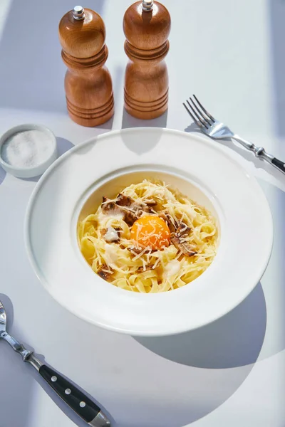 Köstliche Pasta Carbonara serviert mit Besteck, Salz-und Pfeffermühlen auf weißem Tisch im Sonnenlicht — Stockfoto