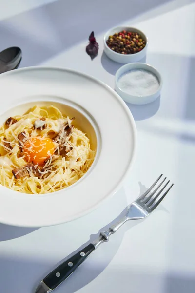 Köstliche Pasta Carbonara serviert mit Besteck und Gewürzen auf weißem Tisch im Sonnenlicht — Stockfoto