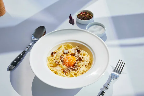 Köstliche Pasta Carbonara serviert mit Besteck und Gewürzen auf weißem Tisch im Sonnenlicht — Stockfoto