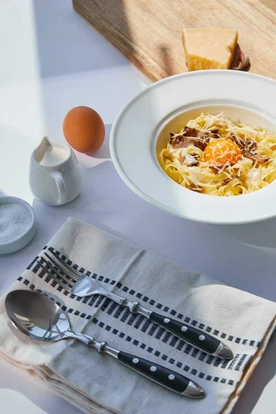 Köstliche Pasta Carbonara serviert mit Besteck, Gewürzen und Zutaten auf weißem Tisch im Sonnenlicht — Stockfoto