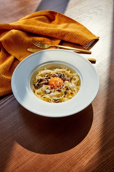 Köstliche Pasta Carbonara serviert mit goldenem Besteck und gelber Serviette auf Holztisch im Sonnenlicht — Stockfoto