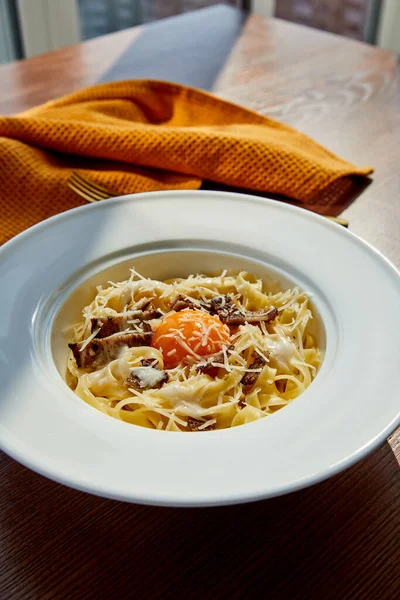 Delicioso macarrão carbonara servido com guardanapo amarelo na mesa de madeira à luz do sol — Fotografia de Stock