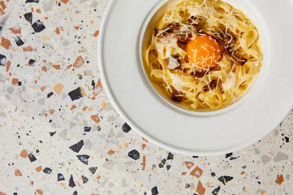 Vue du dessus de délicieuses pâtes carbonara servies dans une assiette ronde sur une table en pierre — Photo de stock