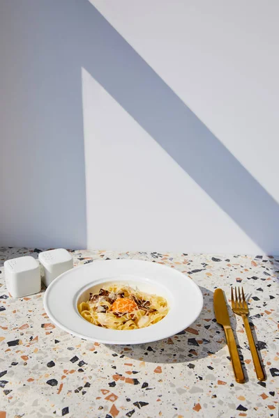 Délicieuses pâtes carbonara servies avec couverts dorés, salière et poivrière sur table en pierre au soleil — Photo de stock