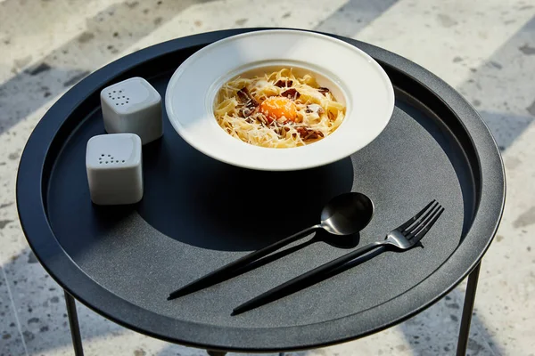 Delicious pasta carbonara served with cutlery, seasoning on black table on marble background in sunlight — Stock Photo