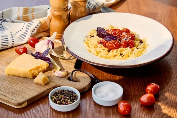 Deliziosa pasta con pomodori servita sul tavolo di legno con tovagliolo, condimento e ingredienti alla luce del sole — Foto stock