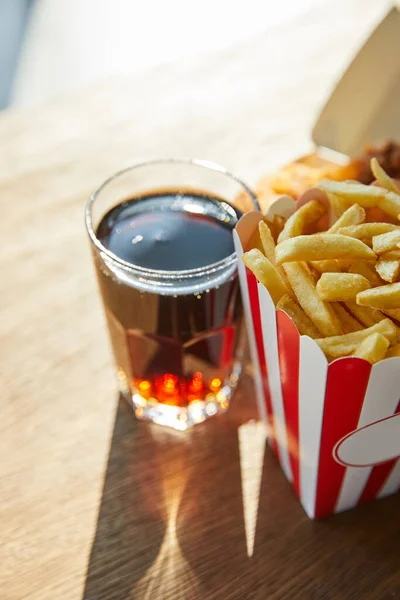 Selektiver Fokus von Pommes frites und Limo im Glas auf Holztisch im Sonnenlicht — Stockfoto