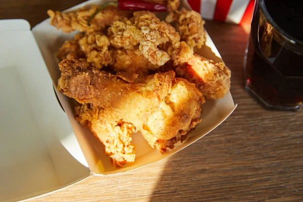 Pollo frito y soda en vidrio sobre mesa de madera a la luz del sol - foto de stock