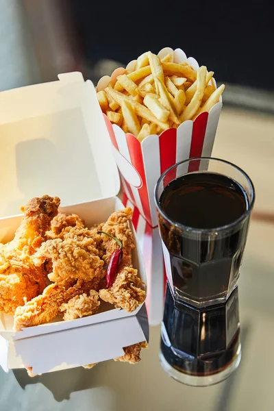 Pollo frito, papas fritas y refrescos en vidrio sobre mesa de vidrio a la luz del sol - foto de stock