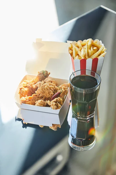 Deep fried chicken, french fries and soda in glass on glass table in sunlight — Stock Photo