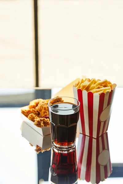 Deep fried chicken, french fries and soda in glass on glass table in sunlight near window — Stock Photo