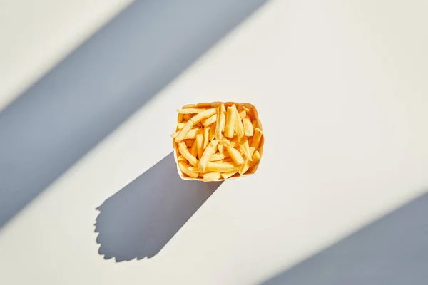 Прекрасный вид на вкусную картошку фри в ведре на белом столе при солнечном свете — стоковое фото