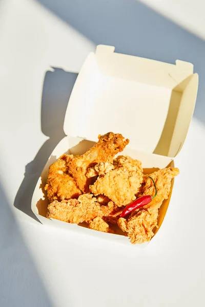 Tasty and spicy deep fried chicken with chili pepper on white table in sunlight — Stock Photo