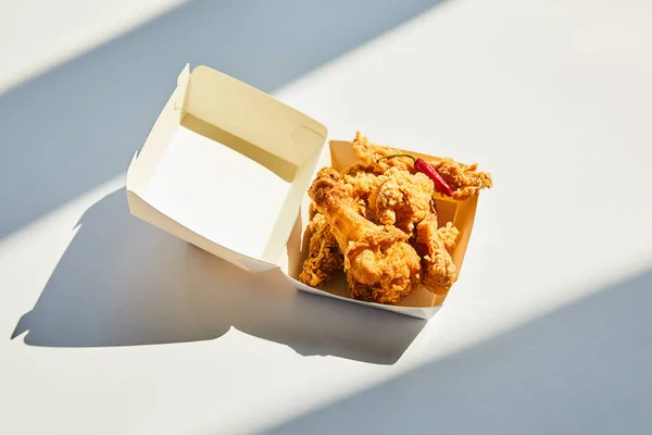 Pollo fritto saporito e piccante con peperoncino sul tavolo bianco alla luce del sole — Foto stock