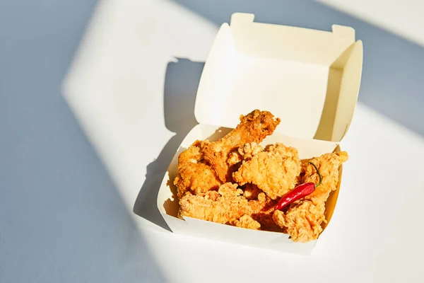 Leckeres und würziges frittiertes Huhn mit Chilipfeffer auf weißem Tisch im Sonnenlicht — Stockfoto