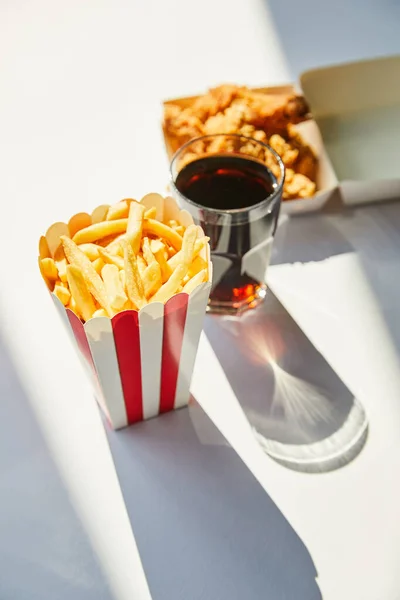 Selective focus of tasty deep fried chicken, french fries and soda in glass on white table in sunlight — Stock Photo