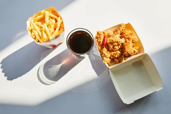 Draufsicht auf leckeres frittiertes Hühnchen, Pommes frites und Limo im Glas auf weißem Tisch im Sonnenlicht — Stockfoto