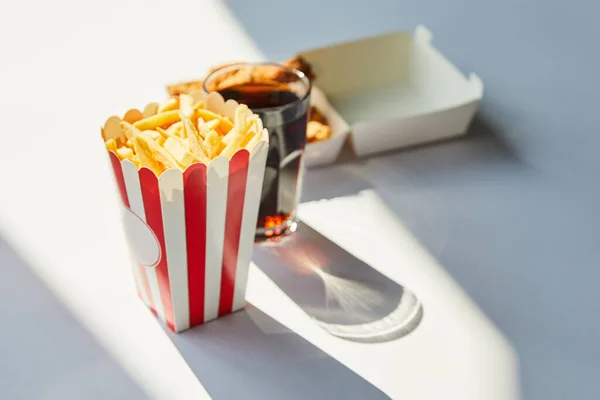 Selektiver Fokus von leckerem frittiertem Hähnchen und Soda im Glas auf weißem Tisch im Sonnenlicht — Stockfoto