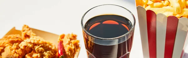 Close up view of tasty deep fried chicken, french fries and soda in glass on white table in sunlight, panoramic crop — Stock Photo