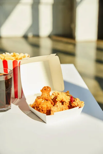 Tasty deep fried chicken, french fries and soda in glass on white table in sunlight — Stock Photo