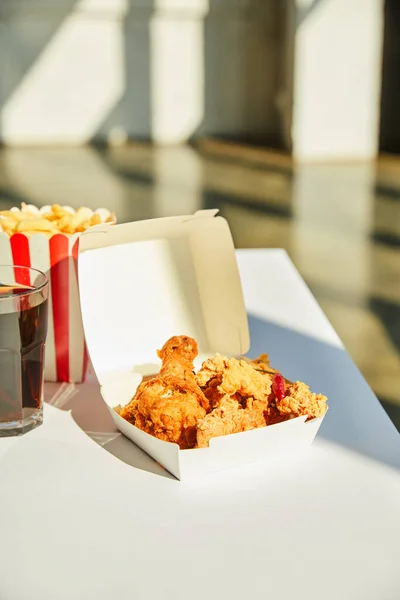 Saboroso frango frito, batatas fritas e refrigerante em vidro na mesa branca à luz do sol — Fotografia de Stock