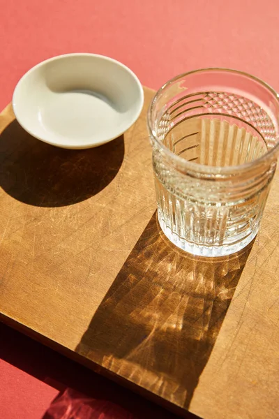 Faceted empty glass and white bowl on wooden board in sunlight — Stock Photo