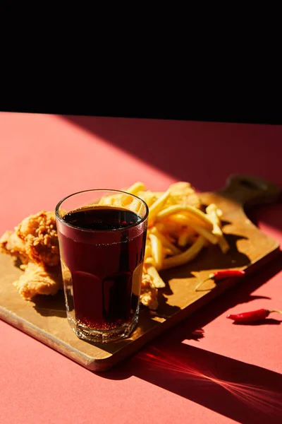 Pollo frito picante y papas fritas servidas en tabla de cortar de madera con soda a la luz del sol aislada en negro - foto de stock
