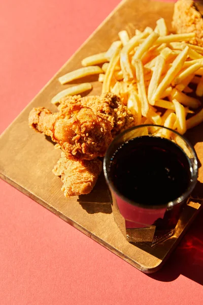 Crispy deep fried chicken and french fries served on wooden cutting board with soda in sunlight — Stock Photo