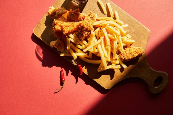 Top view of spicy deep fried chicken and french fries served on wooden cutting board in sunlight — Stock Photo