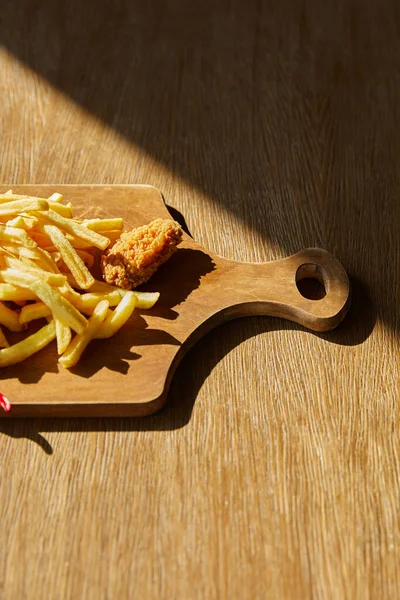 Vista superior de frango frito, batatas fritas a bordo em mesa de madeira à luz do sol — Fotografia de Stock