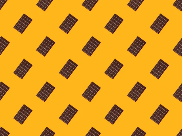 Vista superior de barras de chocolate oscuro dulce sobre fondo de color naranja, patrón sin costuras - foto de stock