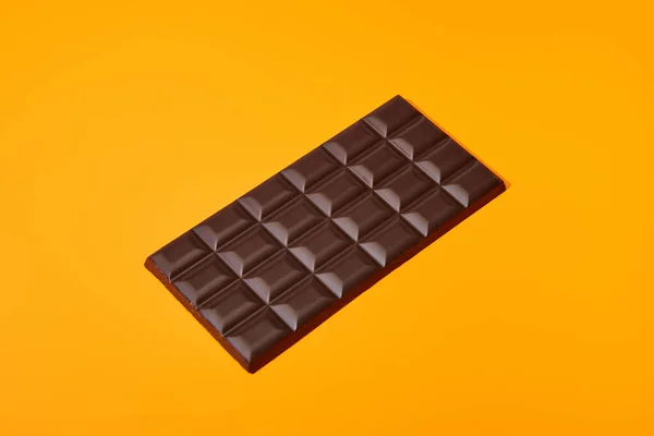 Doce barra de chocolate escuro no fundo colorido laranja — Fotografia de Stock