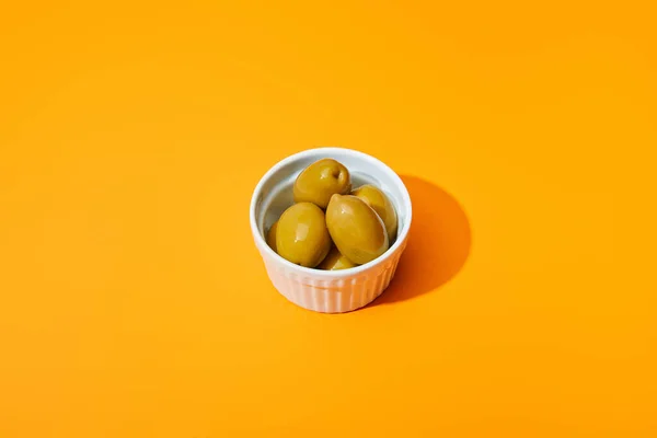 Aceitunas en tazón sobre fondo de color naranja - foto de stock