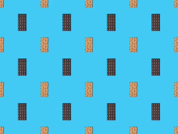 Вид зверху солодких темних шоколадних батончиків і хрустких хлібів на синьому барвистому фоні, безшовний візерунок — стокове фото