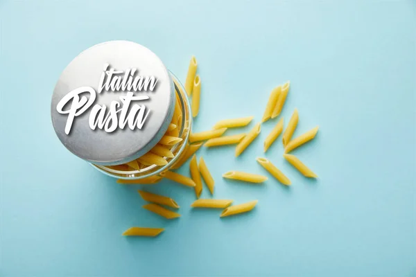 Vue du dessus de la penne crue dispersée du bocal sur fond bleu avec illustration de pâtes italiennes — Photo de stock