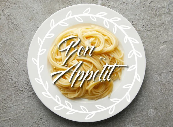 Vista superior de deliciosos espaguetis en placa sobre una superficie de textura gris con ilustración bon appetit - foto de stock
