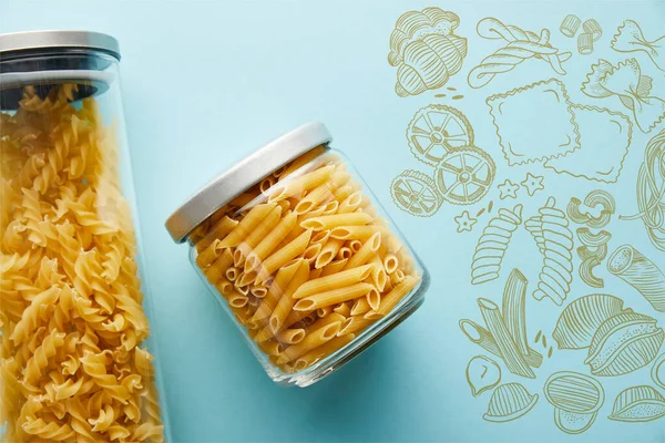 Top view of raw penne and fusilli  in jars on blue background with food illustration — Stock Photo