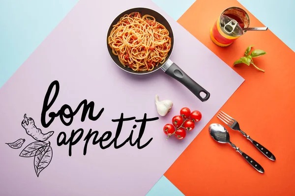 Flat lay with delicious spaghetti with tomato sauce in frying pan near ingredients on red, blue and violet background with bon appetit illustration — Stock Photo