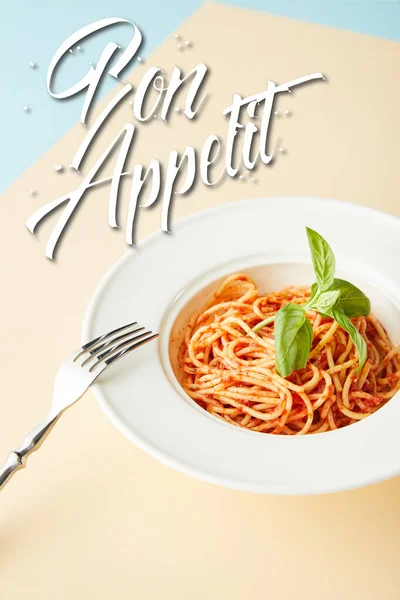 Délicieux spaghettis à la sauce tomate dans une assiette près de la fourchette sur fond bleu et jaune avec illustration bon appétit — Photo de stock