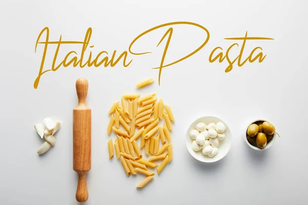 Puesta plana con ajo, rodillo, pasta y cuencos con aceitunas y mozzarella sobre fondo blanco, ilustración pasta italiana - foto de stock