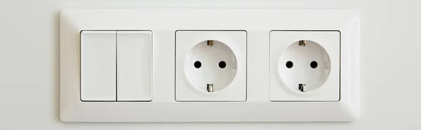 Panoramic crop of power sockets near switch on white wall — Stock Photo