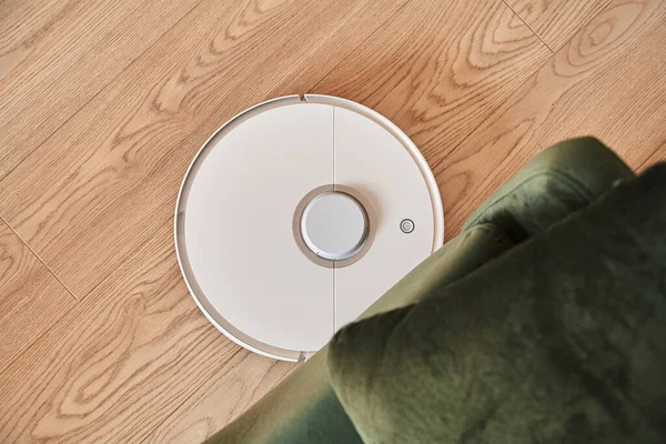 Top view of white robotic vacuum cleaner washing floor near green sofa — Stock Photo