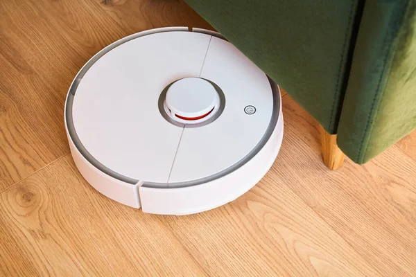 Modern automatic vacuum cleaner washing floor near green sofa — Stock Photo