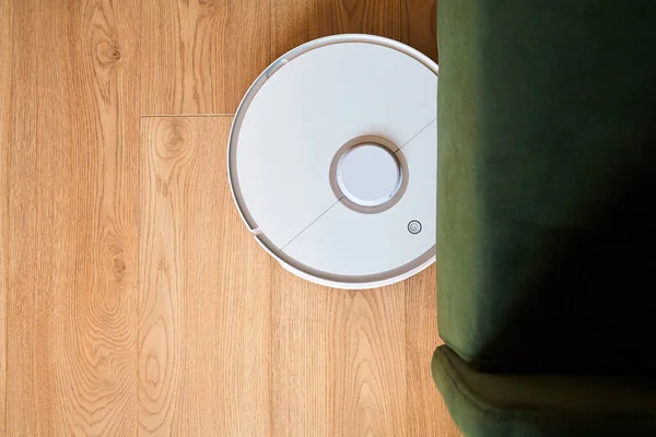 Top view of modern automatic vacuum cleaner washing floor near sofa — Stock Photo