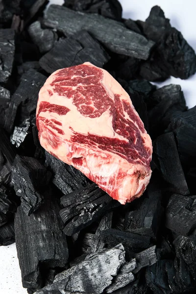 Bistecca cruda su carboni neri su fondo bianco — Foto stock