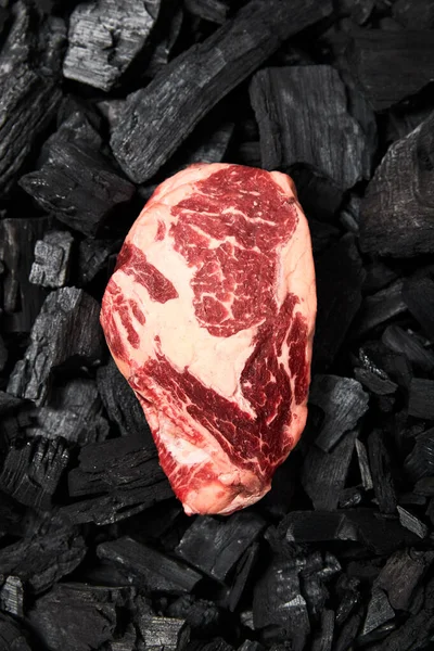 Vue de dessus du steak cru frais sur les charbons noirs — Photo de stock