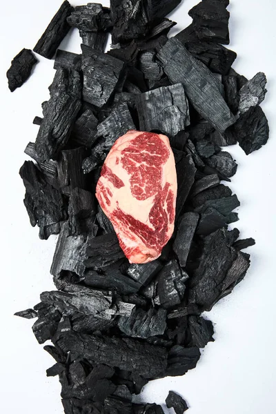 Top view of fresh raw steak on black coals on white background — Stock Photo