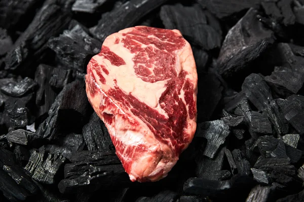 Vue de dessus du steak cru frais sur les charbons noirs — Photo de stock