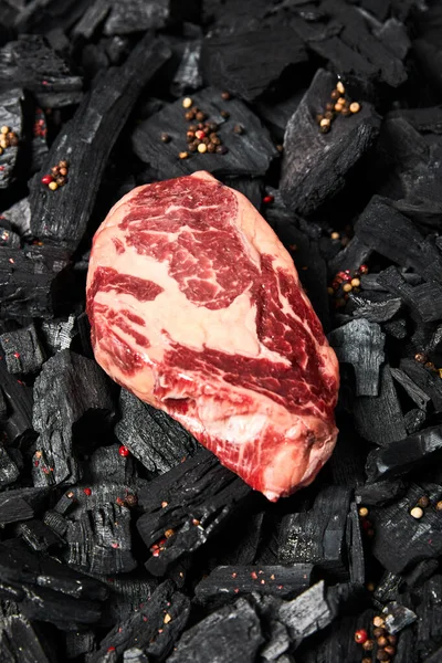 Draufsicht auf frisches rohes Steak auf Schwarzkohle mit Pfefferkörnern — Stockfoto