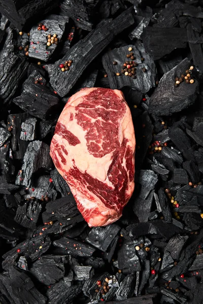 Vista dall'alto di bistecca fresca cruda su carboni neri con grani di pepe — Foto stock